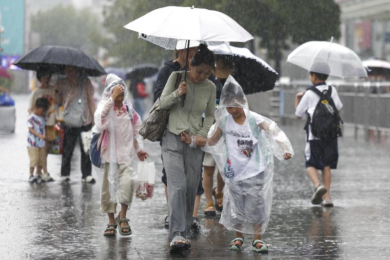  7月30日，旅客在上海站南广场冒雨前行。
