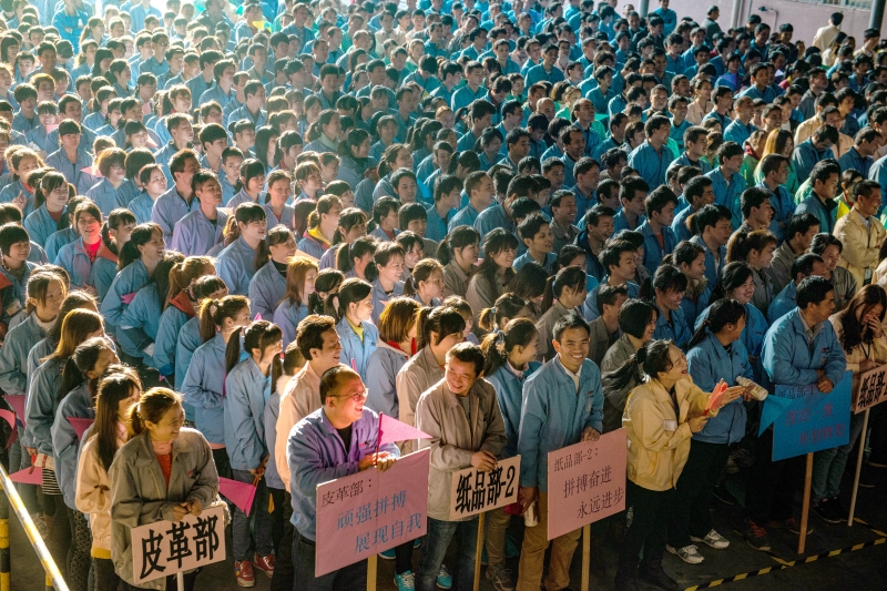 2015年12月31日， 广东东莞，某纸品厂的员工参加运动会，数万人站在空地上，肩连着肩、脚挨着脚，横是一条线，竖是一列队，老板站在台上，用大喇叭点评全厂工作。