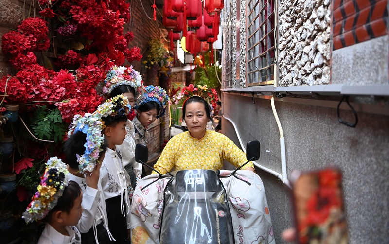 蟳埔村，一名蟳埔女骑电动车从几名体验簪花围的游客前经过    新华社图