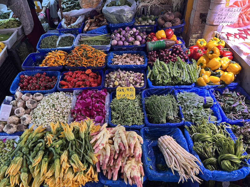 地州山茅野菜专卖店售卖的菜蔬品种繁多,照片中可见草芽、海菜花、南瓜花、臭菜(羽叶金合欢)、夜来香花蕾、玫瑰花瓣、茉莉花、百合、四棱豆、新鲜的涮涮辣……  摄影/半夏